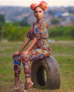 African girl in ankara jumpsuit and headwrap, sitting on a tyre
