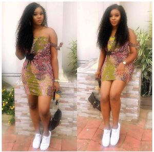African girl in trendy off-shoulder Ankara dress style with white sneakers