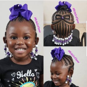 Happy little black girl with natural hair cornrowed into a half up half down style, embellished with purple hair bows and beads