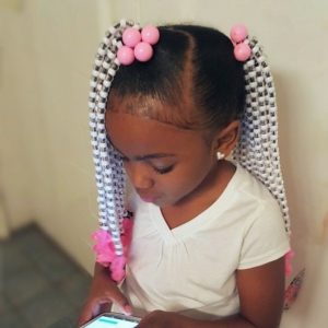 Little black girl with hair styled into two ponytails covered in accessories