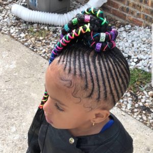 Little black girl with her hair cornrowed into a ponytail of braids adorned with colorful strings and metals