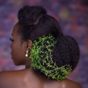 model wearing kinky low bun with green floral accessory