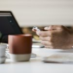 hand with mobile phone, laptop and mug