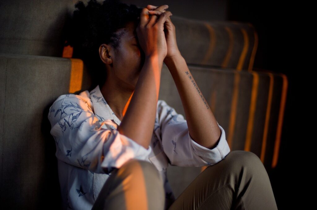 how to reduce stress and sleep better- black woman sitting in dimly lit room